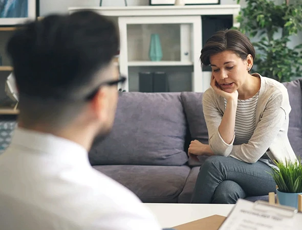 A woman sitting on a couch engaged in a supportive emotional intelligence coaching session with a professional consultant, demonstrating emotional awareness and professional confidence.