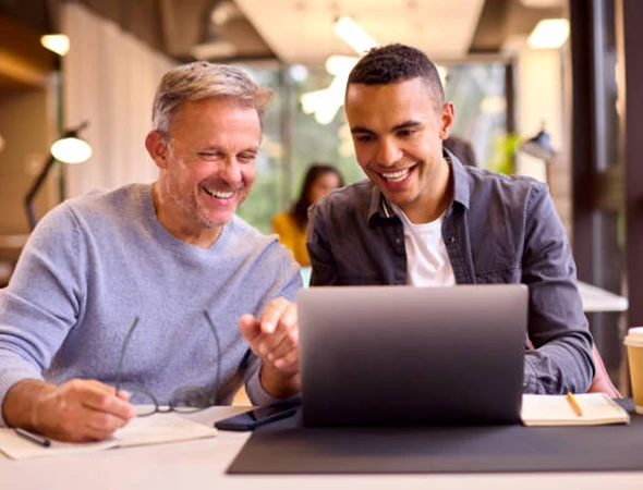 Two professional men smiling while working together on a laptop, illustrating a resilience habit-building program in Charlotte, North Carolina.