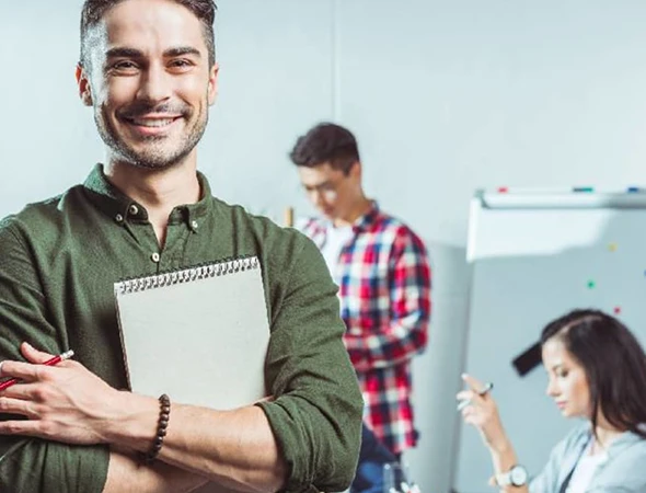A smiling male professional holding a notebook, representing goal achievement coaching in Indianapolis, IN.